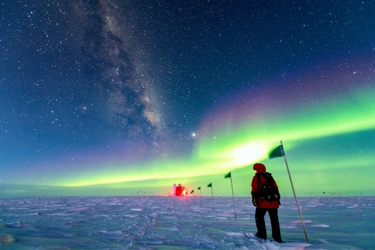 a bundled up person in the snow with the neon green glow of an aurora overhead