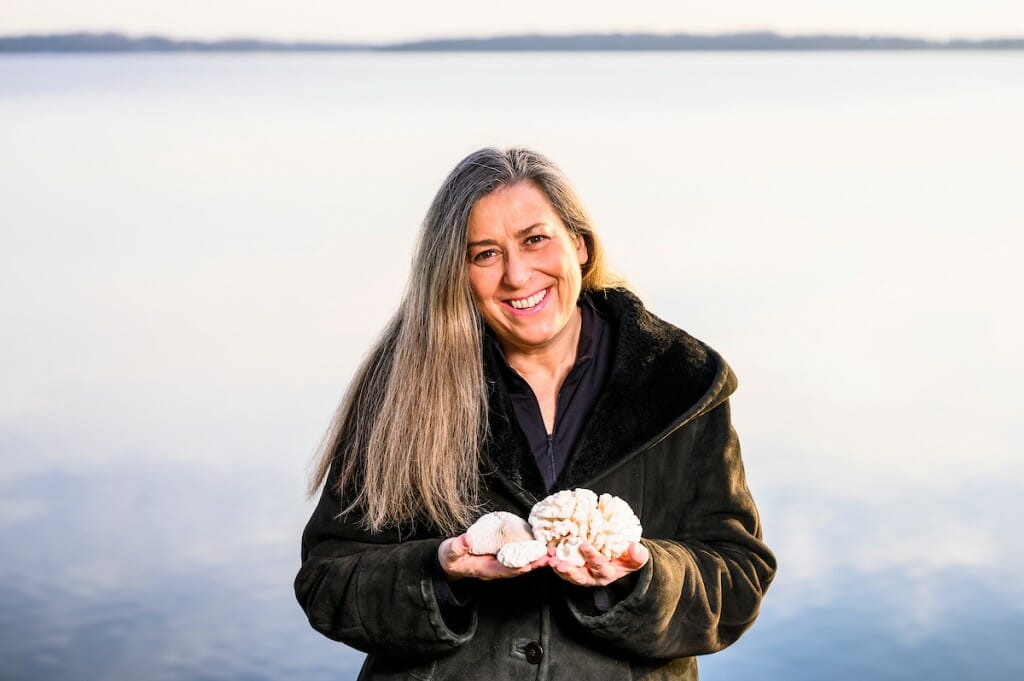 A woman holding two coral species stands in front of a body of water