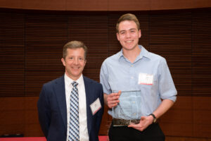 a man on the left with a man on the right holding a clear glass plaque