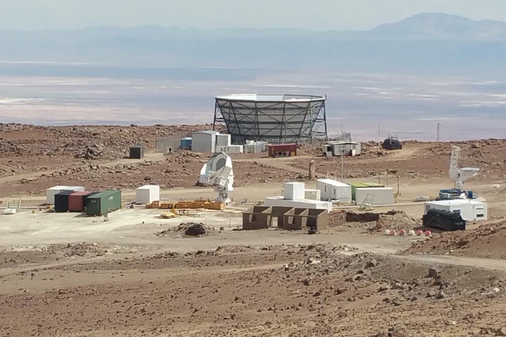 a desert scene with a hazy valley in the background and building equipment and structure that looks like a cone with the pointed end chopped off as the center focus
