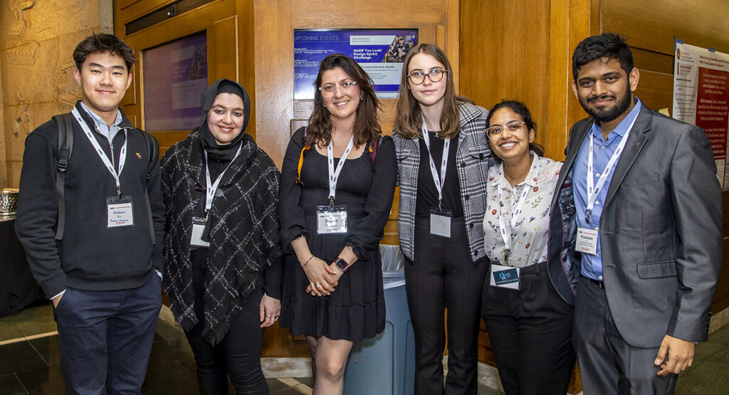 a group of people in business attire stand and pose in a line, they all have nametag lanyards around their necks