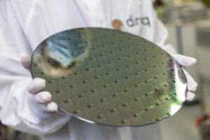 hands from an unidentified individual hold a metal pancake-like object with some tech-y designed on it. The object is roughly a foot in diameter.