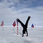 a person on top of a snowy expanse with different countries flags behind her does a handstand