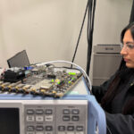 a woman wearing safety goggles works on a tech-y computer-like piece of equipment